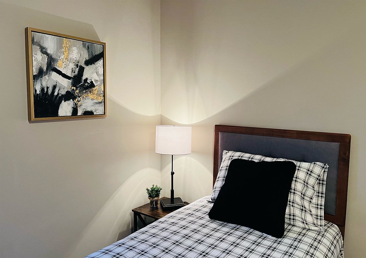 A bedroom with a bed , nightstand , lamp and painting on the wall.