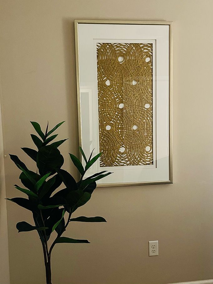 A picture is hanging on a wall next to a plant.