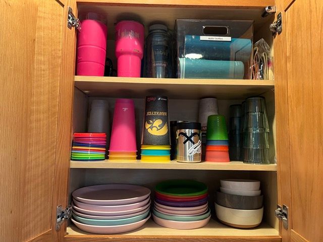 A kitchen cabinet filled with plates , cups , and bowls.