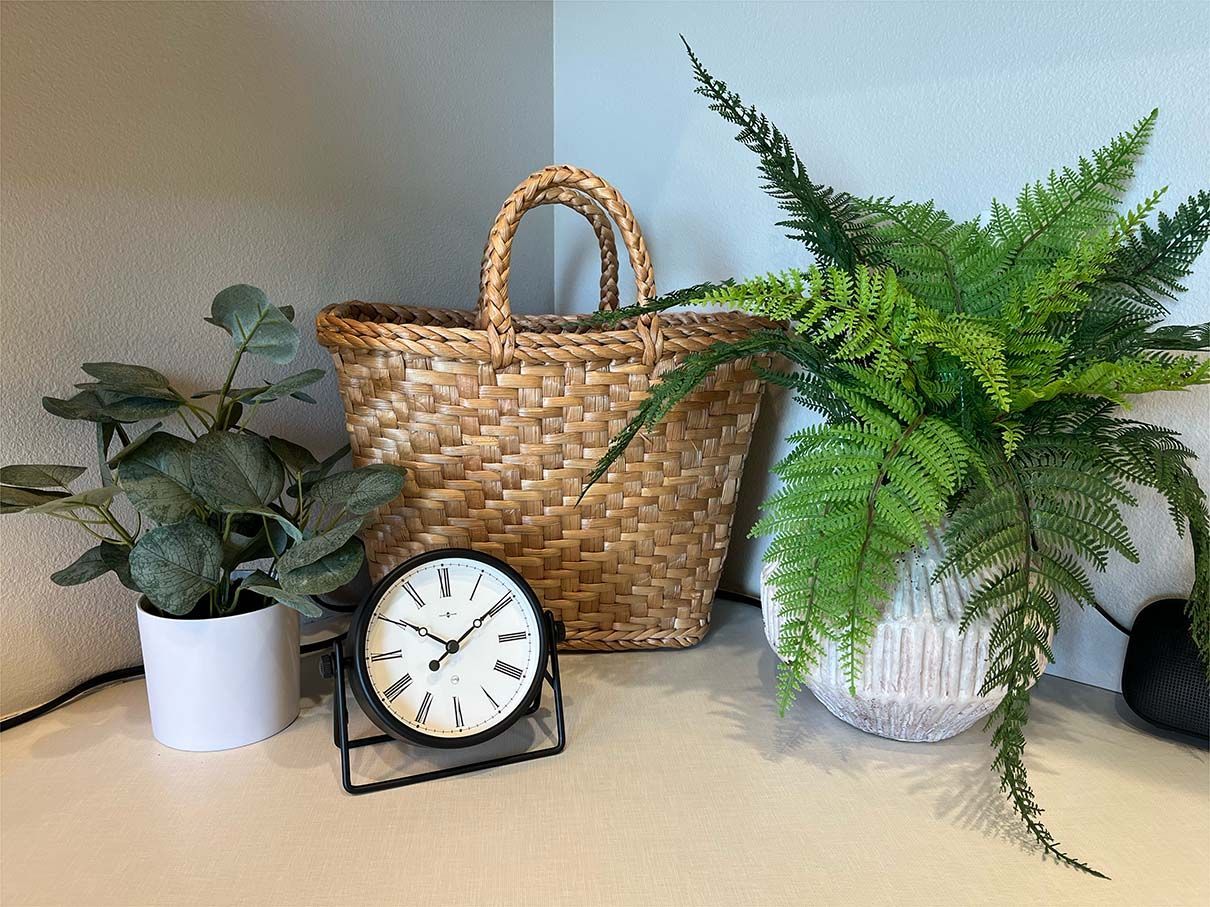 A clock is sitting on a table next to a basket and potted plants.