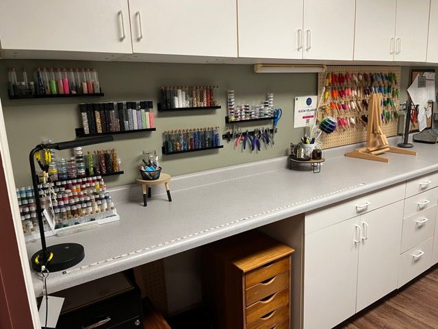 A craft room with a desk , cabinets , shelves and a lamp.