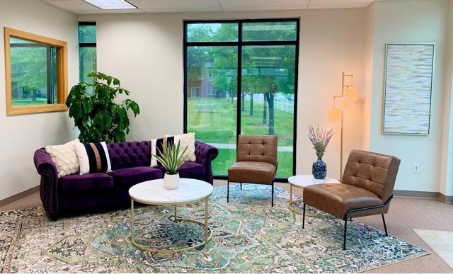 A living room with a purple couch , two chairs , a coffee table and a large window.