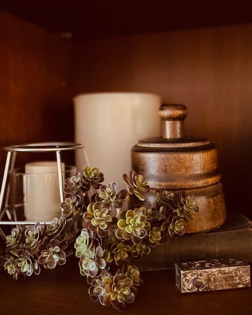 A shelf with a vase , candle , and succulents on it.