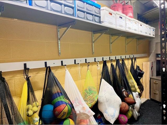 A bunch of balls are hanging on hooks under a shelf