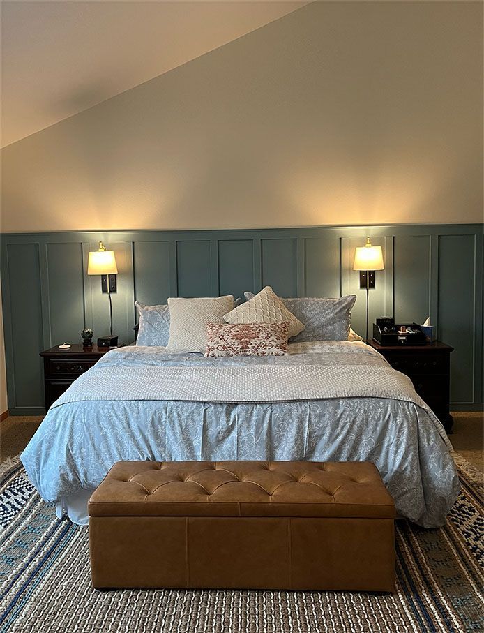 A bedroom with a king size bed and a brown ottoman.