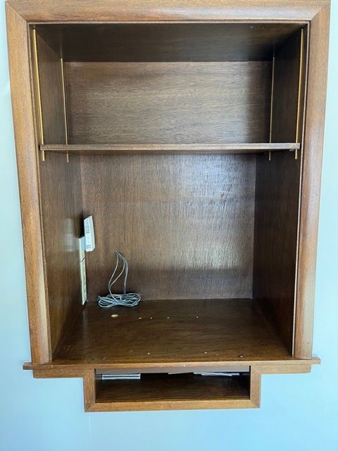 An empty wooden shelf with a cord plugged into it.