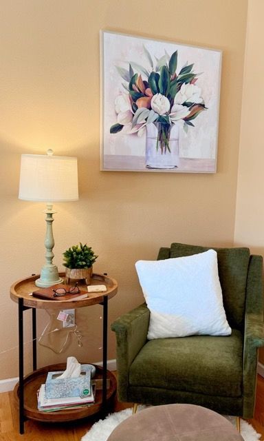A living room with a chair , table , lamp and a painting on the wall.
