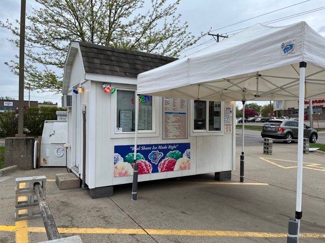 A small white ice cream shop with a white tent in front of it