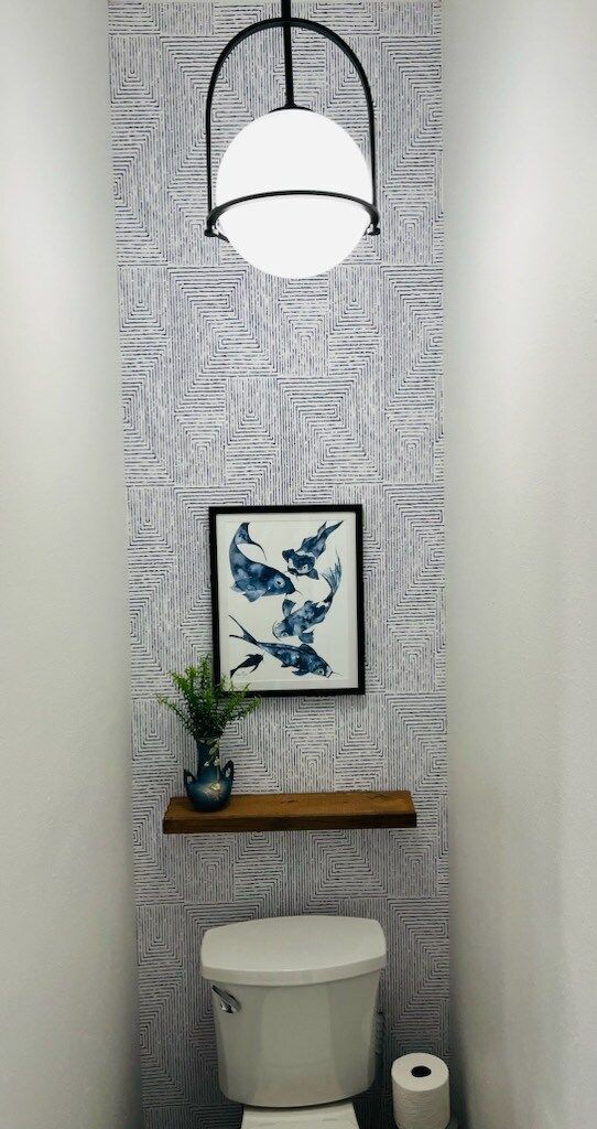 A bathroom with a toilet , shelf , light and picture on the wall.