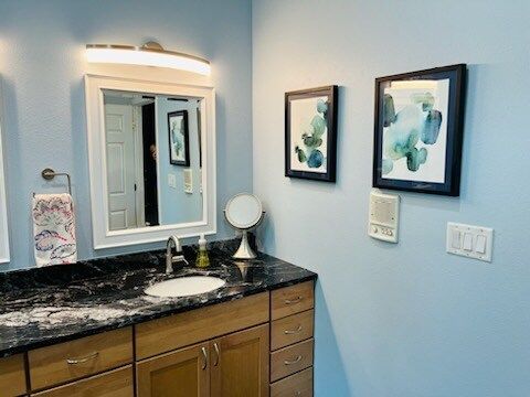 A bathroom with a sink , mirror , and two paintings on the wall.