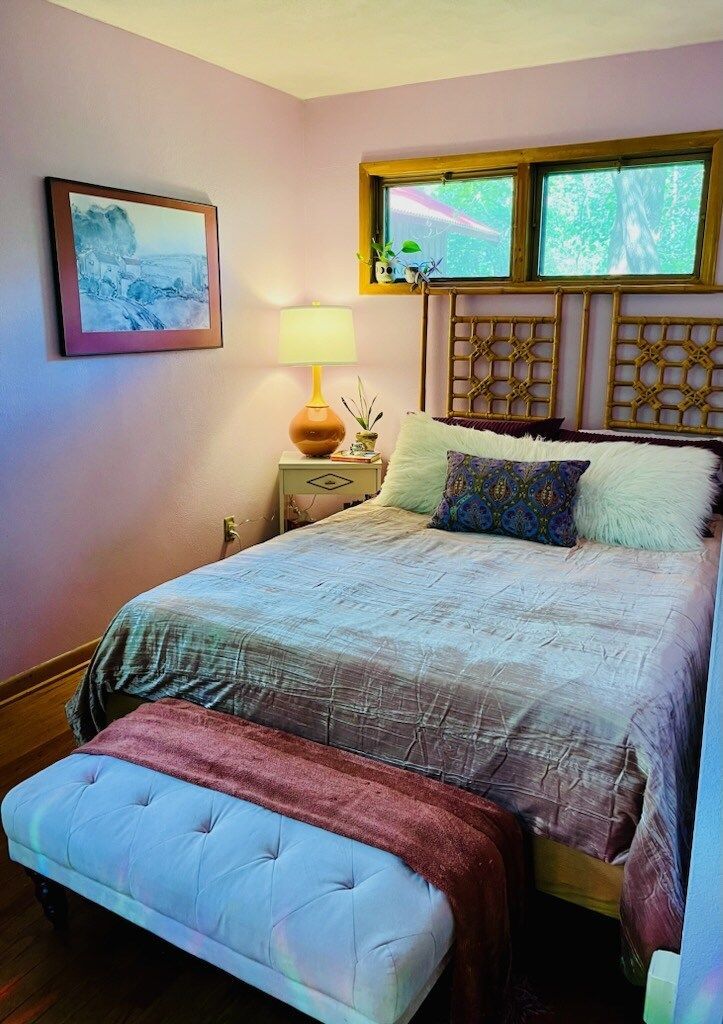 A bedroom with a bed , nightstand , lamp and window.