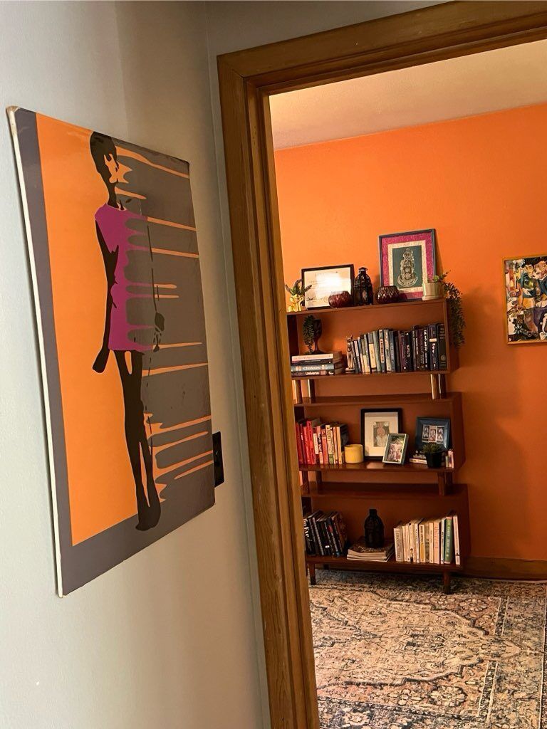 A painting of a woman is hanging on a wall next to a bookshelf.