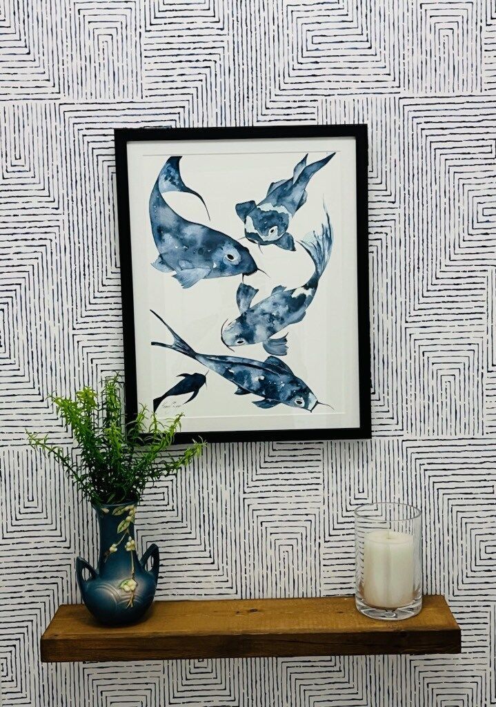 A framed painting of birds hangs on a wall next to a vase and candle