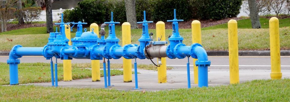 Blue water pipes and valves with yellow safety bollards on grass.