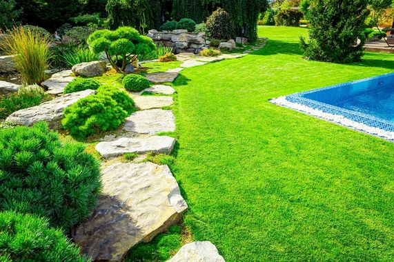 Lush green lawn borders a flagstone path, garden beds, and a pool with blue cover.