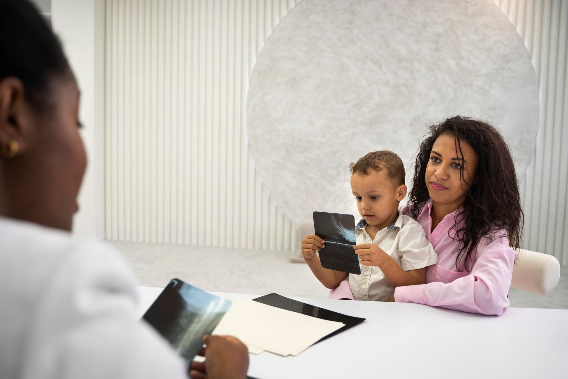 A woman is holding a baby while sitting at a table with a doctor.