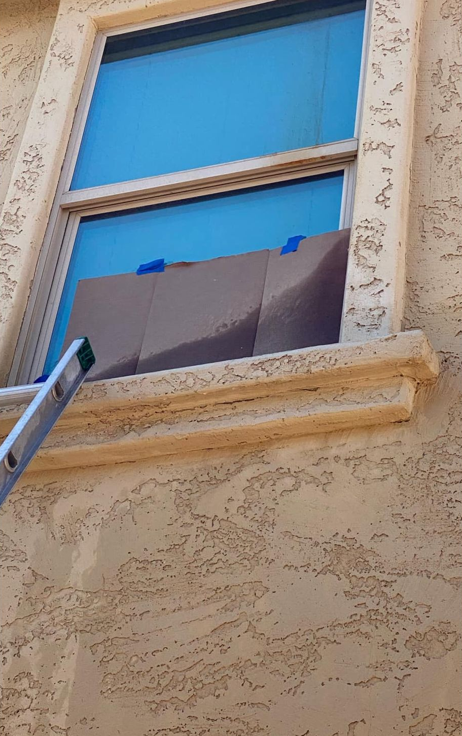 Person cleaning a window with spray bottle and cleaning tool outside a building.