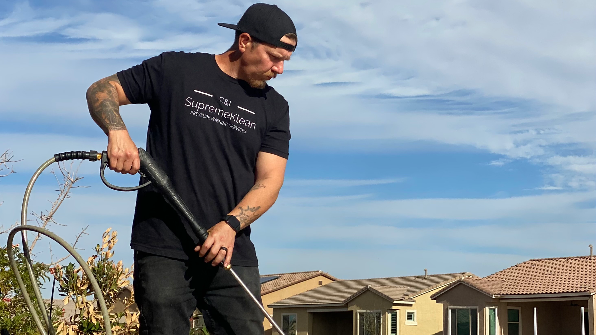 Man in black shirt and hat using a cleaning tool on a rooftop, sunny day.