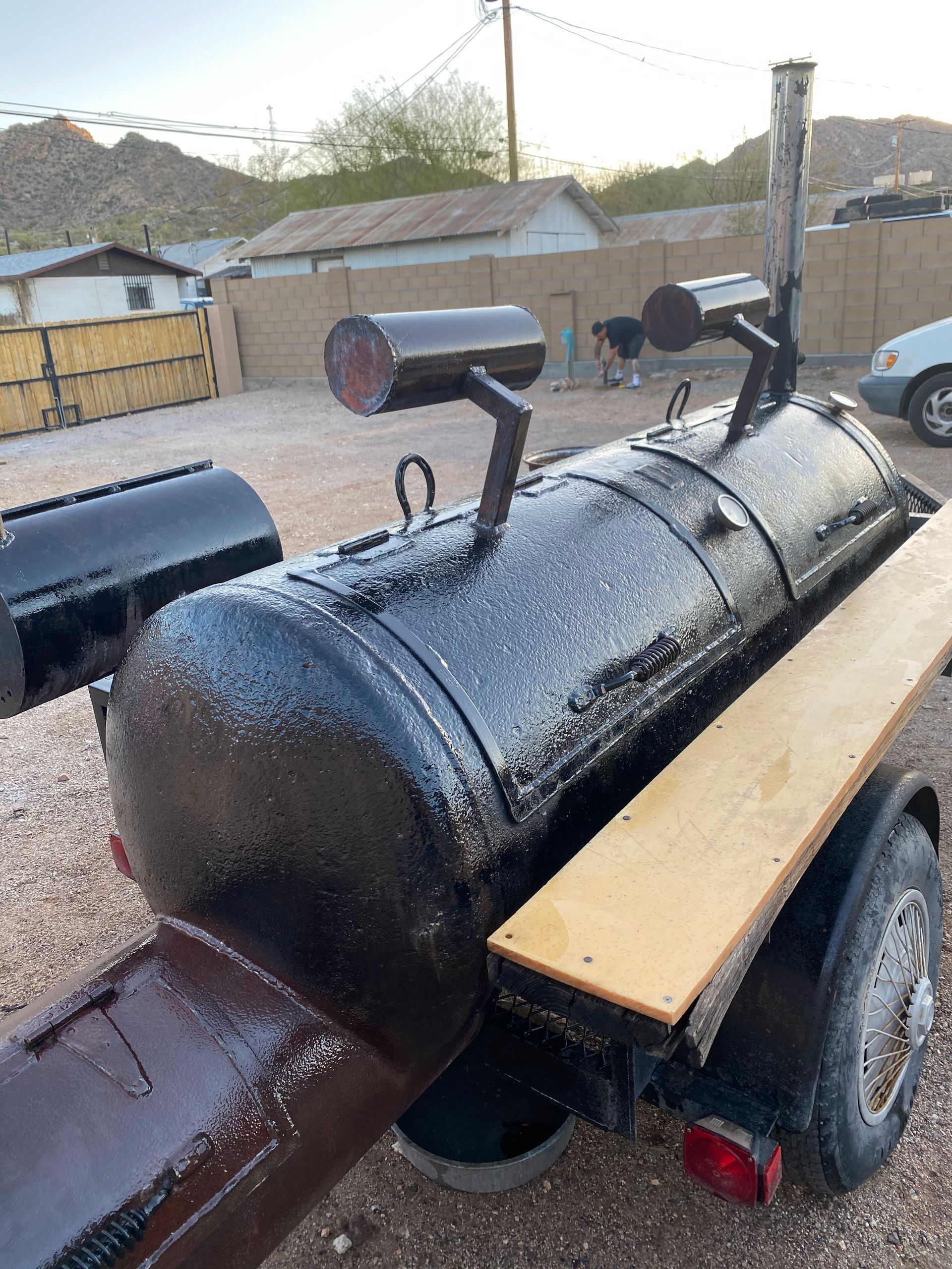 Black smoker on a trailer, with two smokestacks, wooden shelf, and red light.