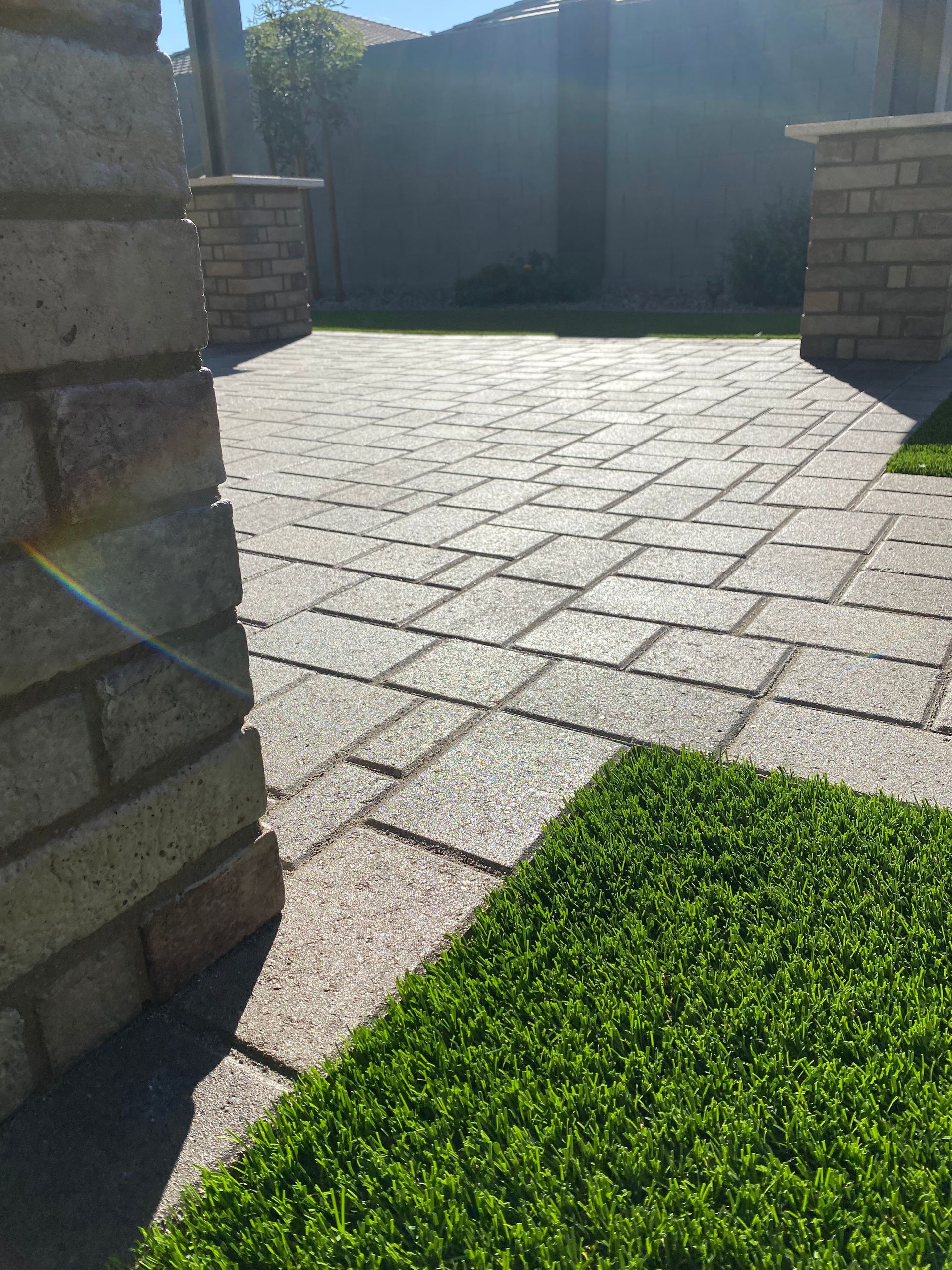 Brick patio with artificial turf, bordered by brick columns, on a sunny day.