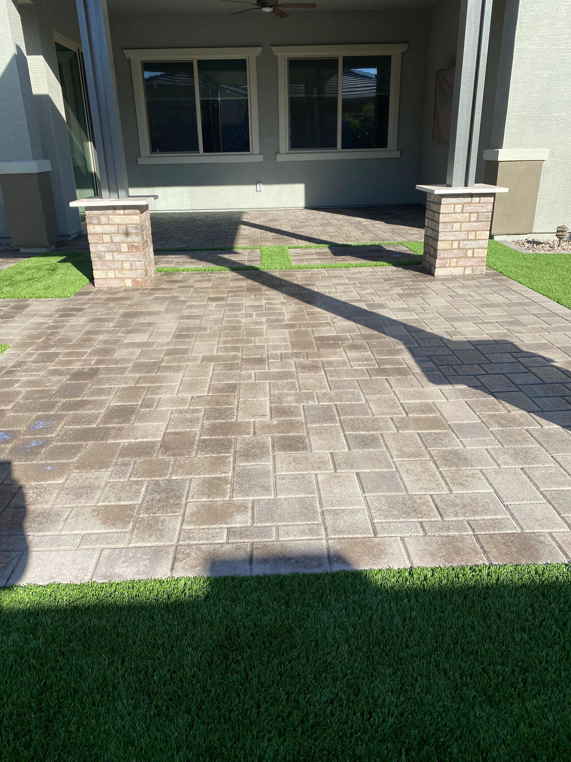 Brick patio leading to a covered porch with two square pillars, green grass surrounds the patio.