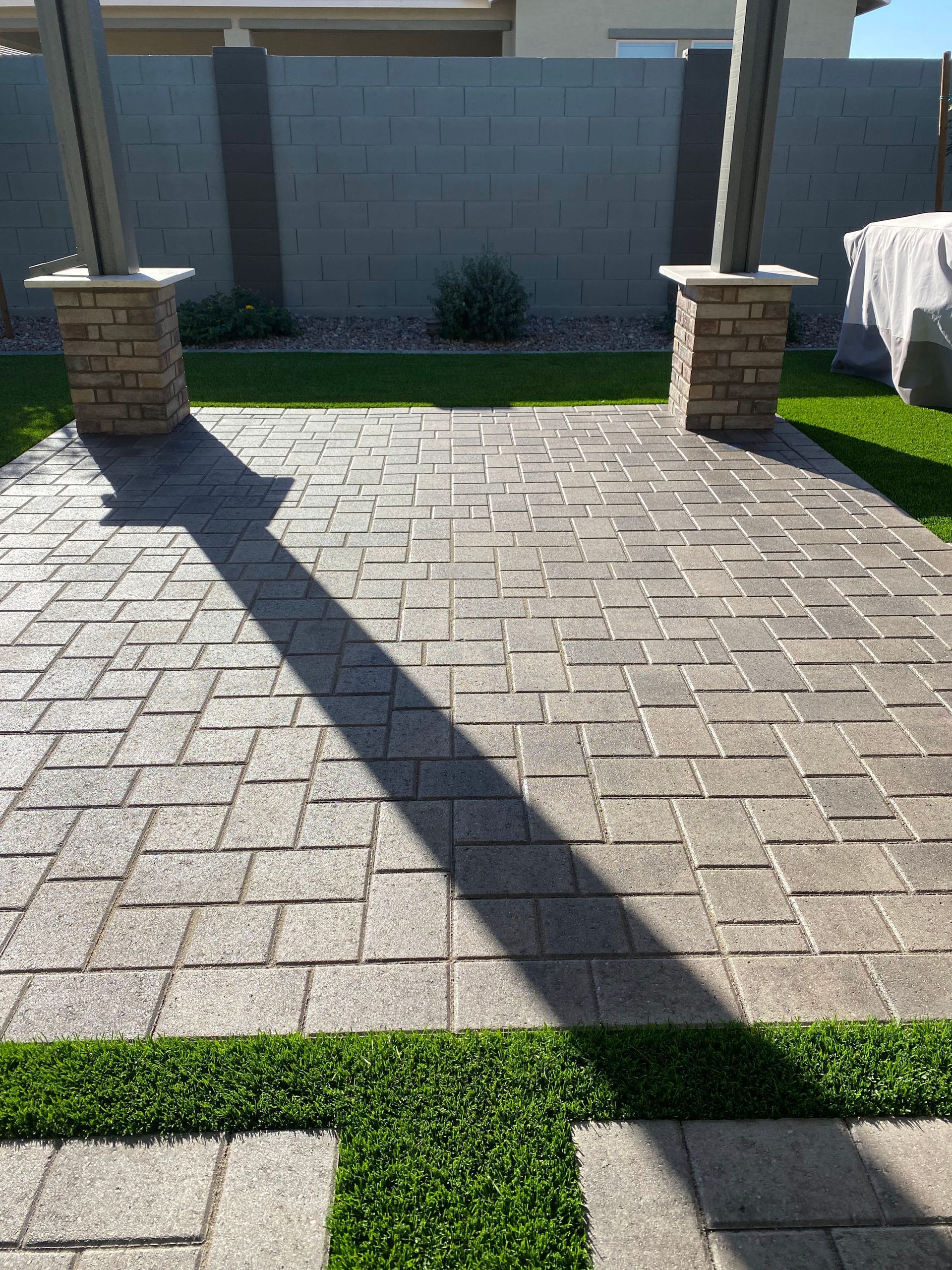 Paver patio with two brick columns, green grass, and a gray wall backdrop.
