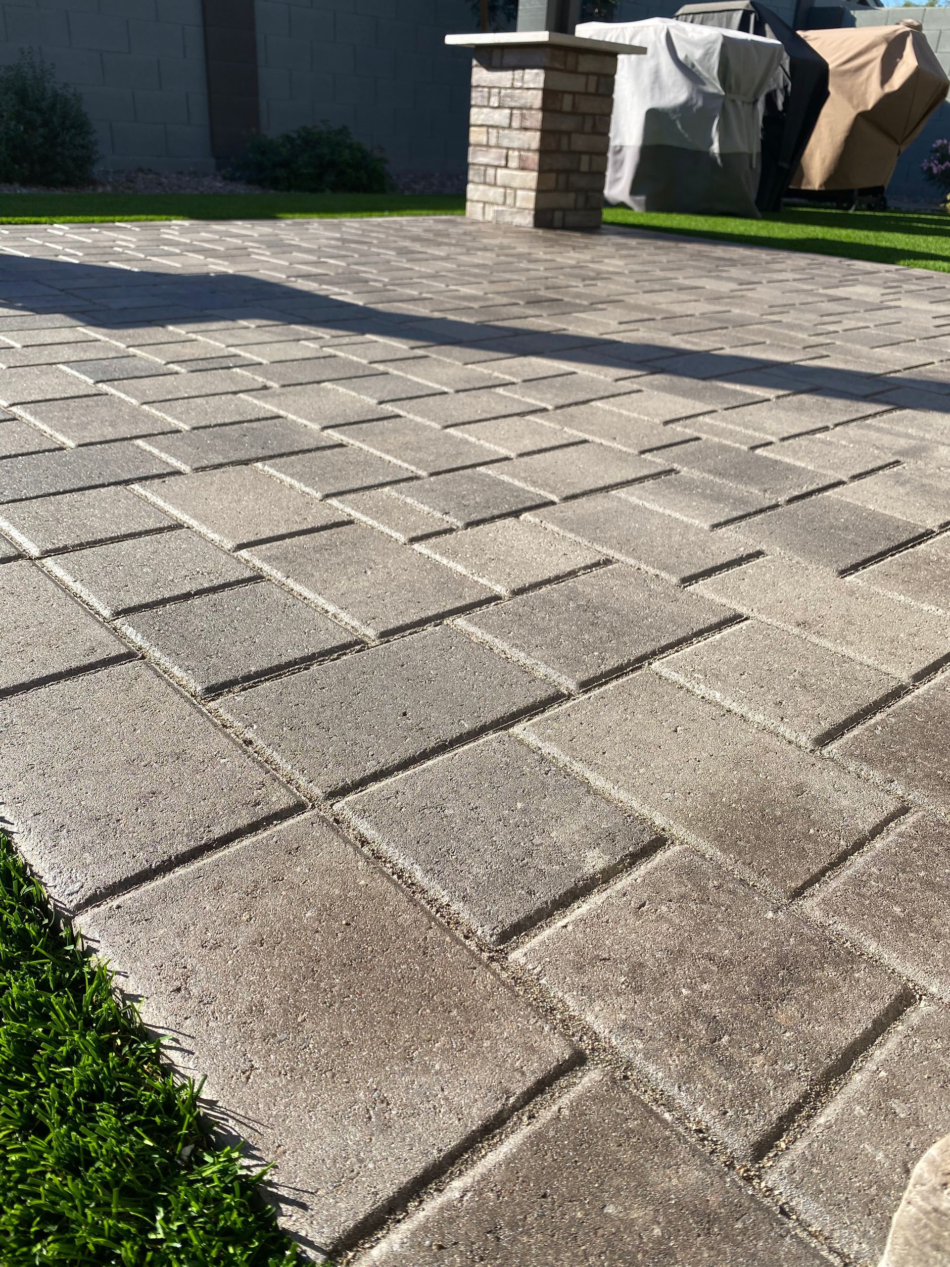 Stone brick patio with a column in the background and green grass on the side.