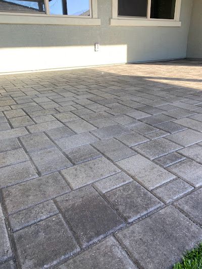 Brick patio with a repeating pattern, gray bricks under a building.