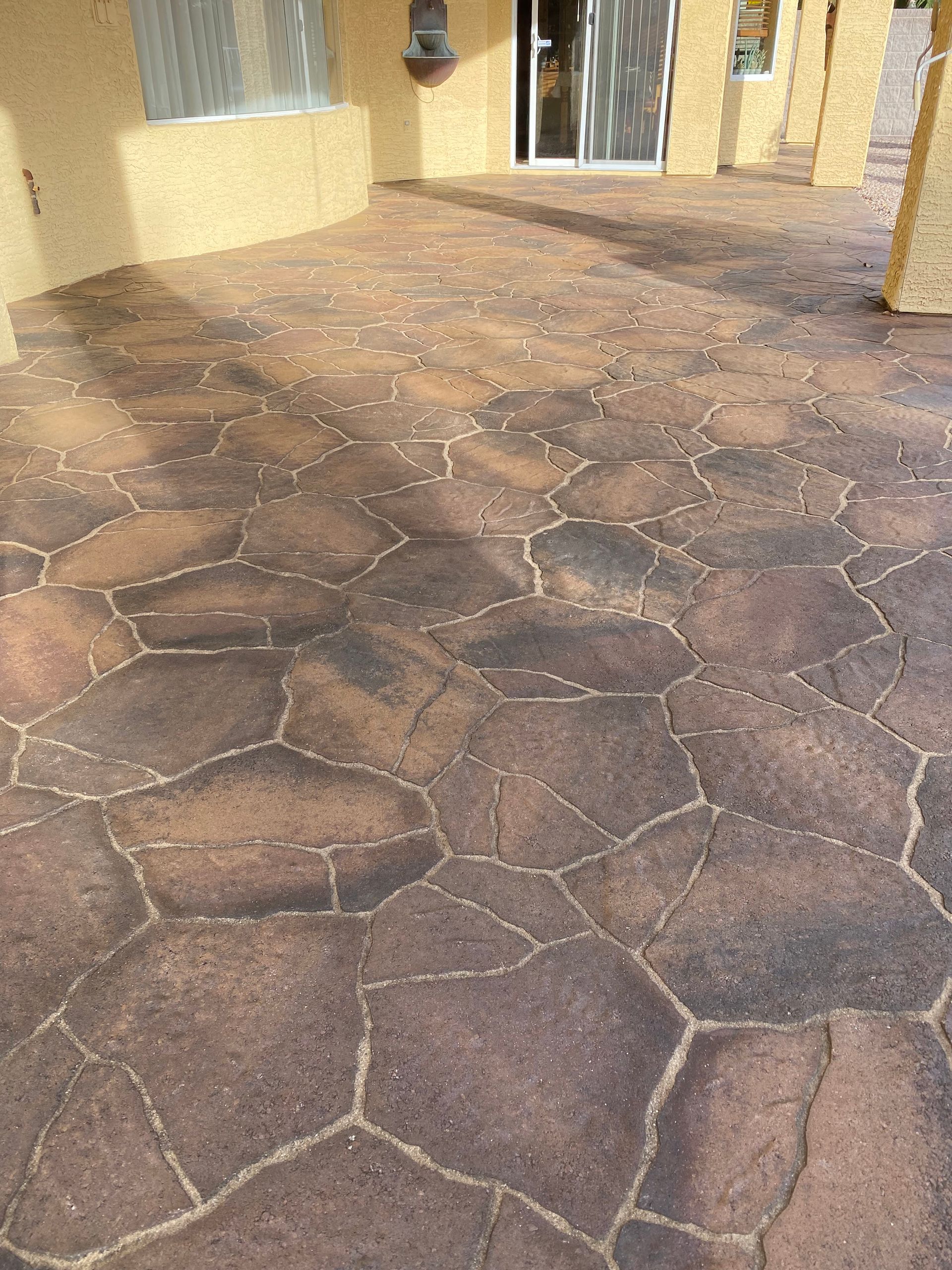 Stone-patterned patio with brown and tan coloration, near a sliding glass door and building columns.