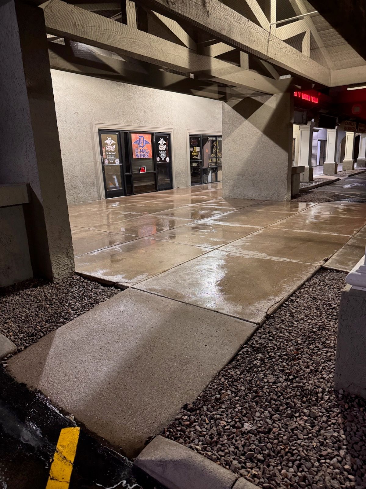 Wet concrete entrance to a building. Two dark doors visible. Overhead support beams. Pebbles line the bottom.