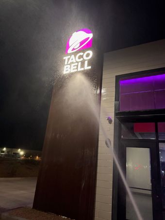 Taco Bell sign being washed at night; water spraying, dark setting, purple and white logo.