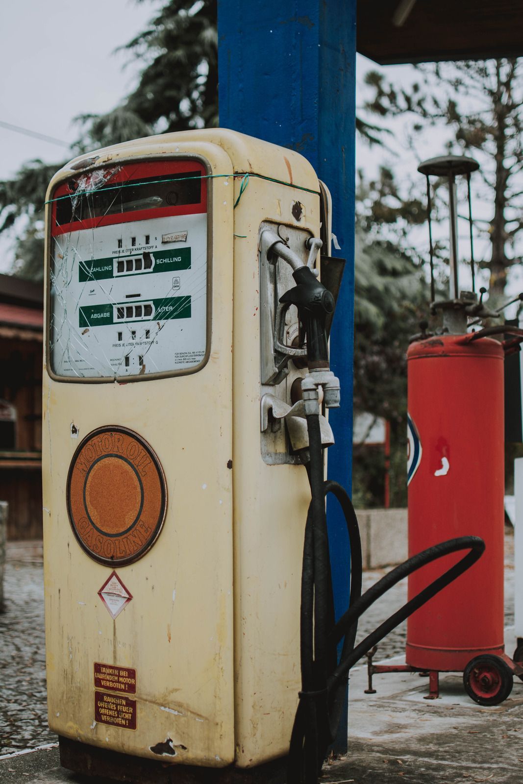 Vintage, weathered gas pump; yellow, red, and blue, outside, next to a red fire extinguisher.