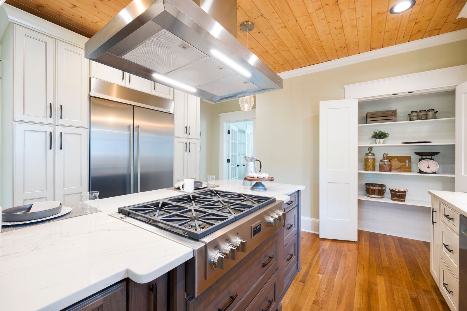 Modern kitchen with stainless steel appliances, white cabinets, wood ceiling and floors.