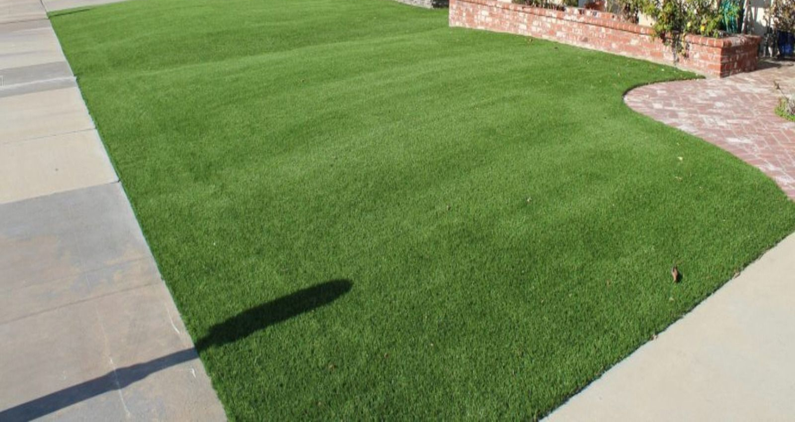 Green artificial turf lawn next to a concrete sidewalk and brick wall.