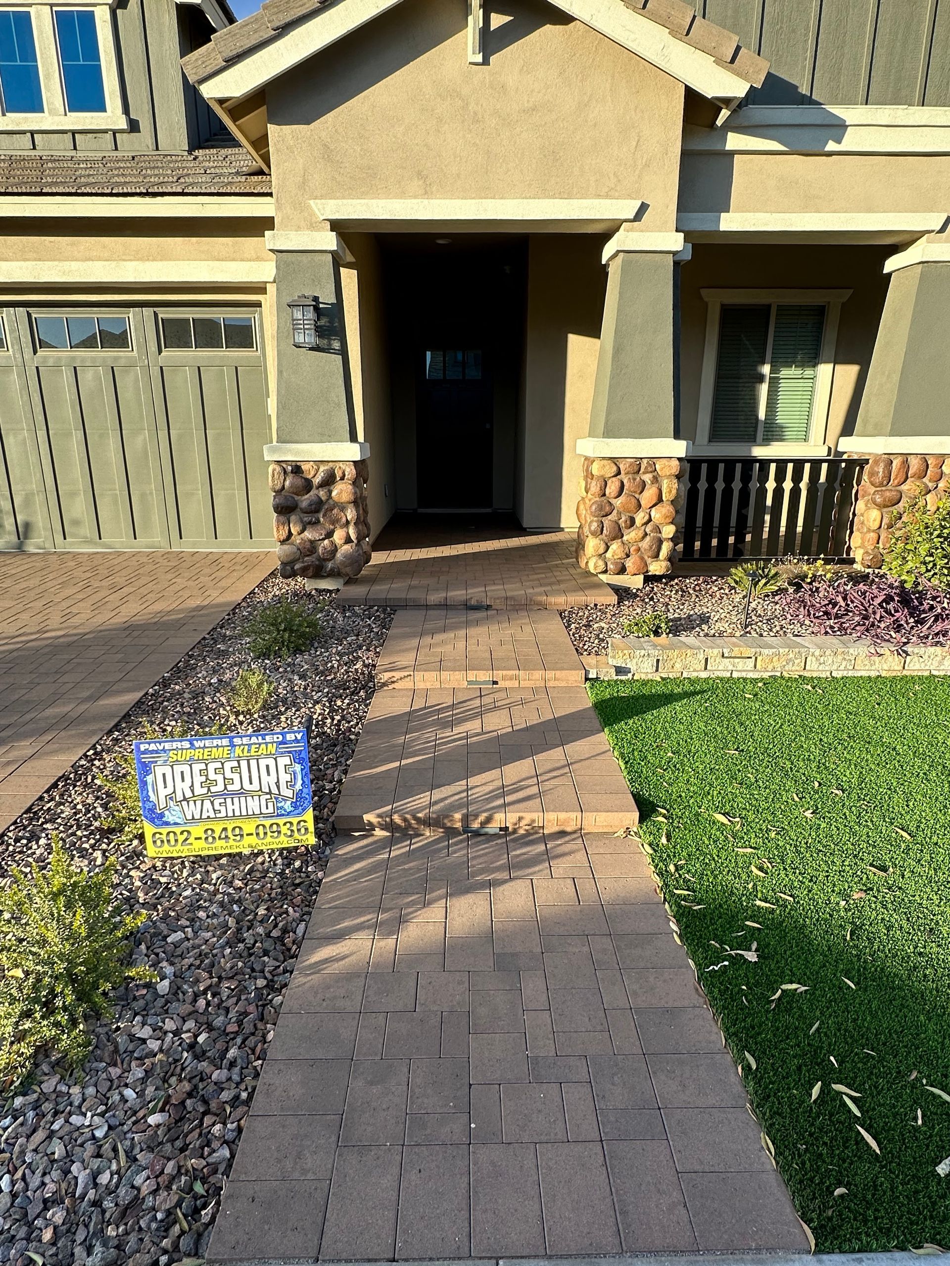 Brick walkway leading to a house with a tan exterior and a green lawn.
