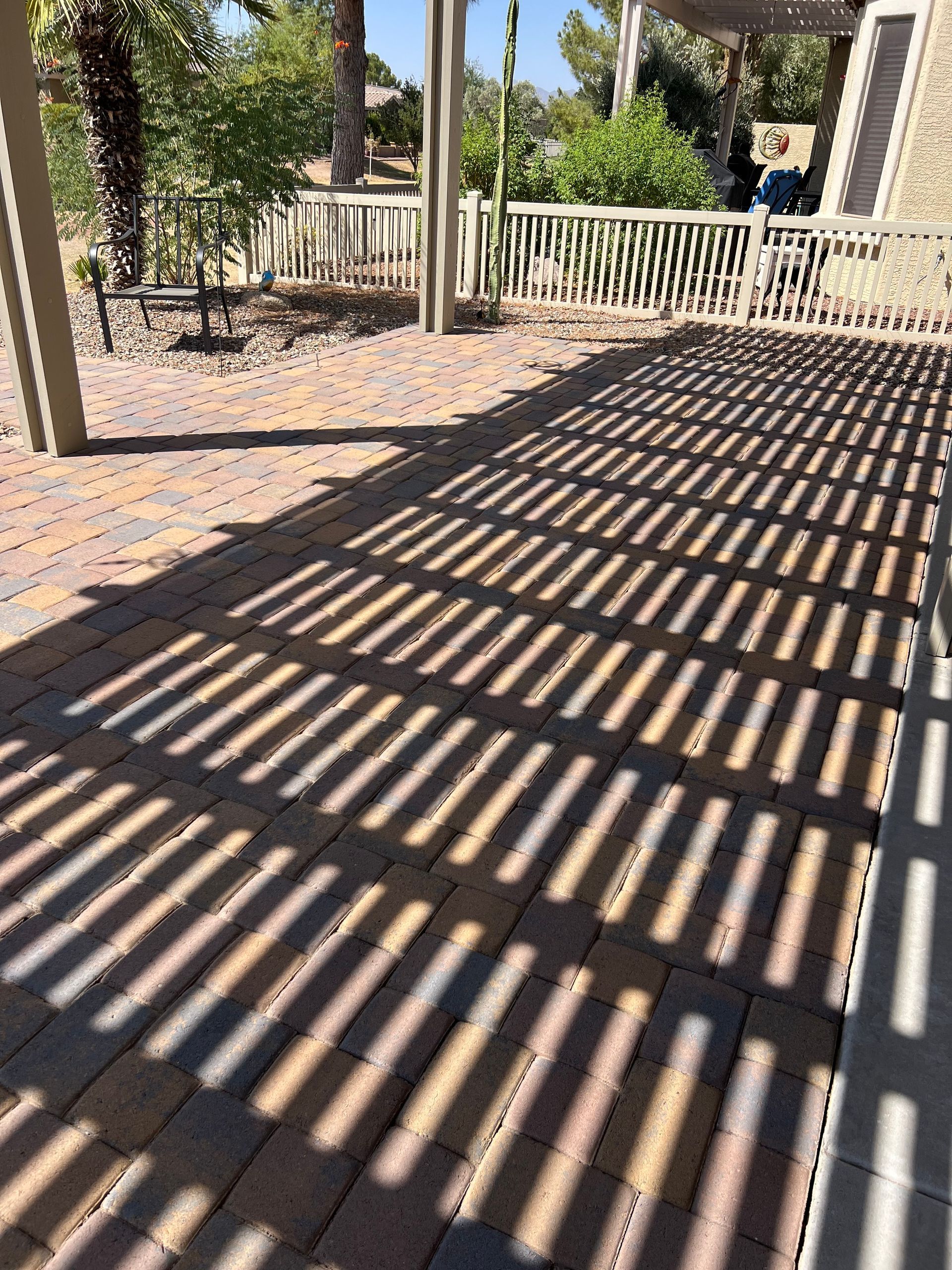 Patio with brick pavers and overhead trellis casting striped shadows in sunlight.