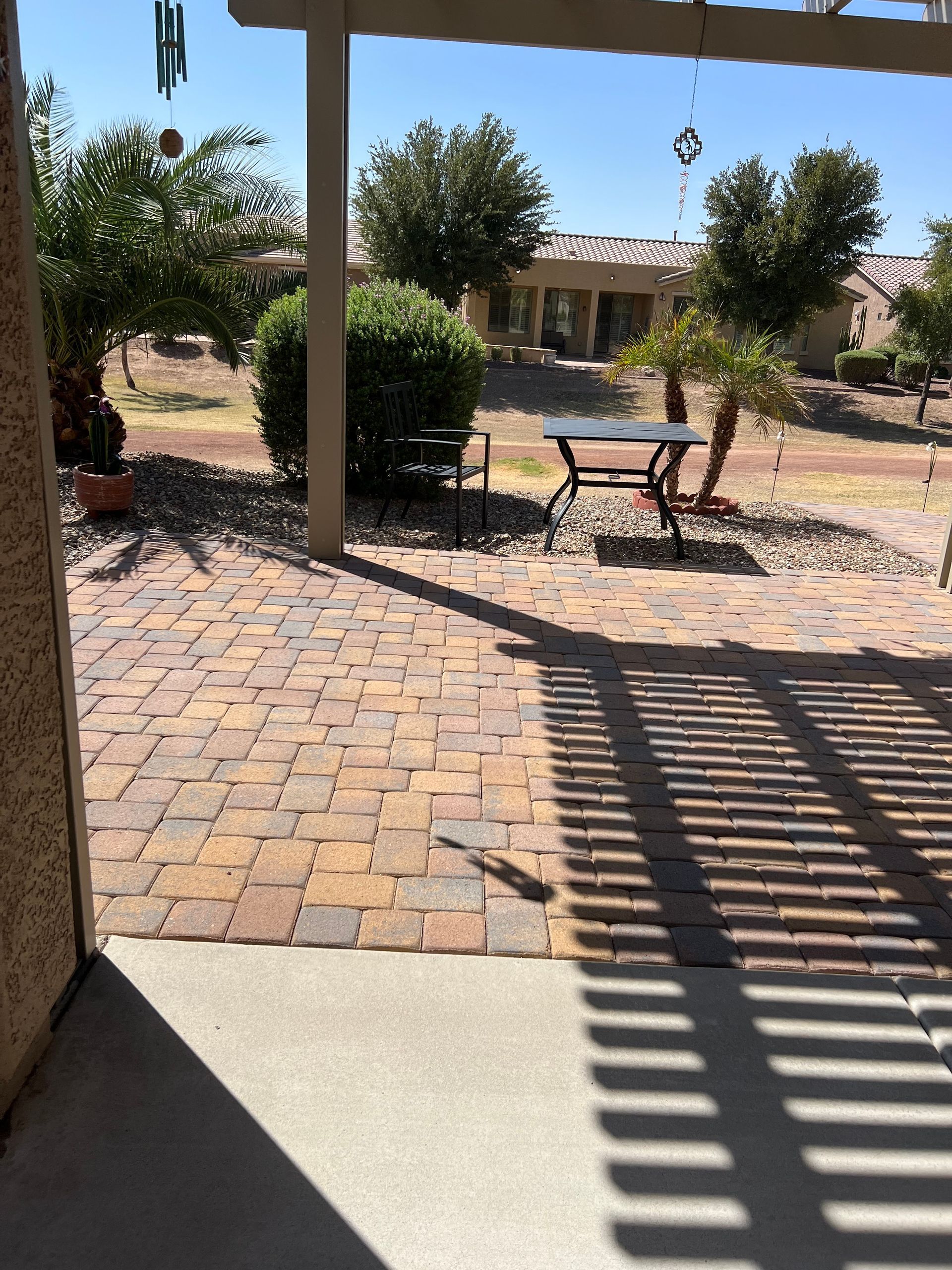 Patio with brick pavers, table, and pergola casting shadows on sunny day.