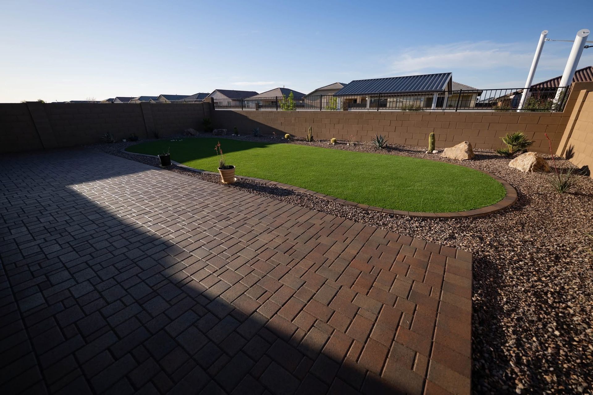 Backyard patio with brick paving, lawn, and gravel landscaping under a blue sky.