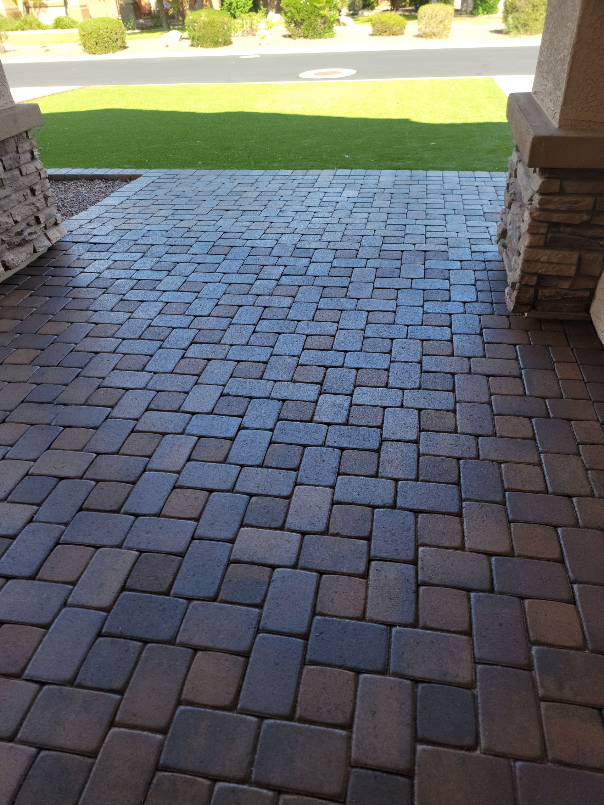 Brick pavers on a porch, brown and gray, leading to a street and green lawn.
