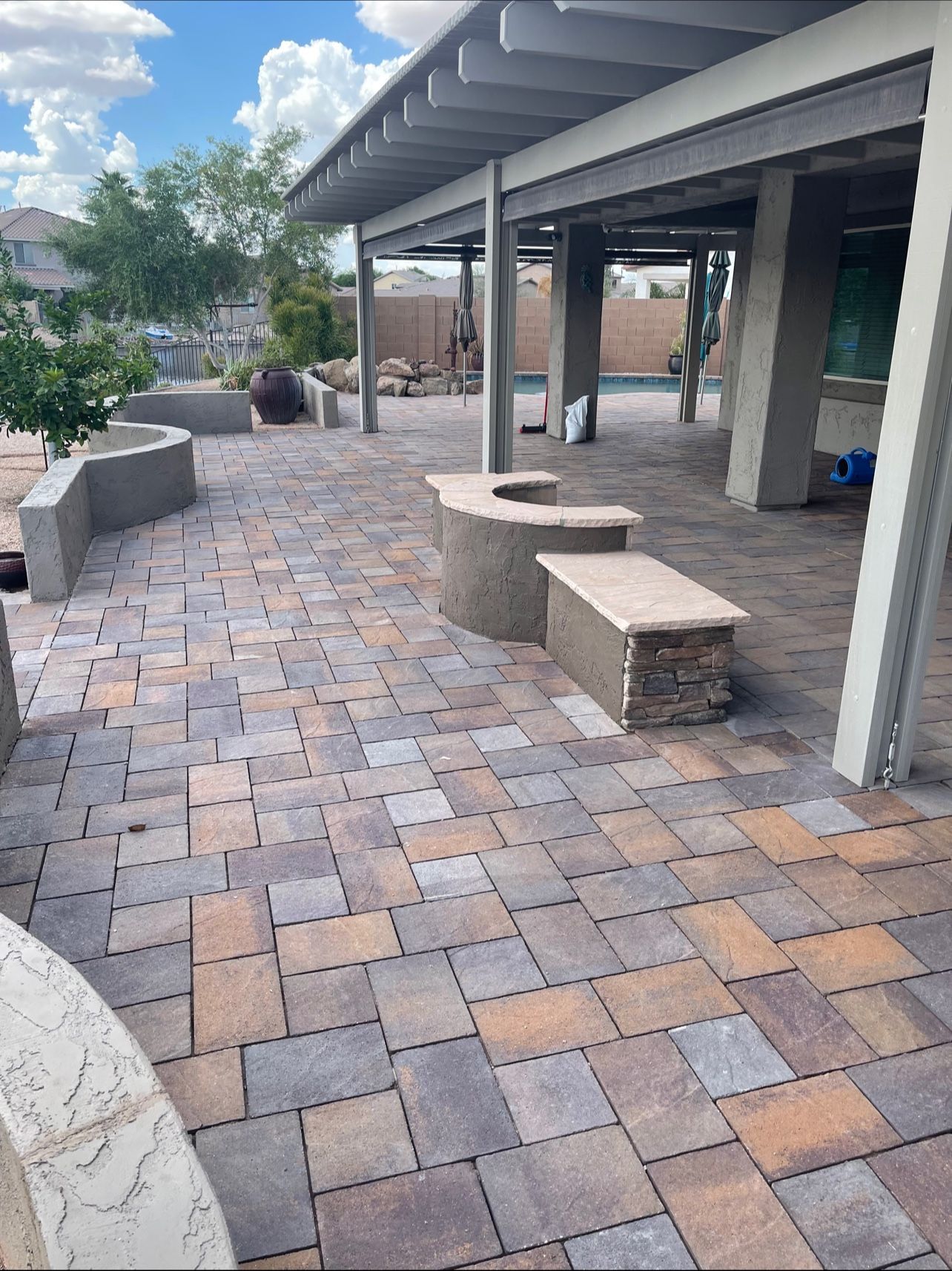 Brick patio with built-in seating under a covered patio with pillars. Multi-colored bricks.