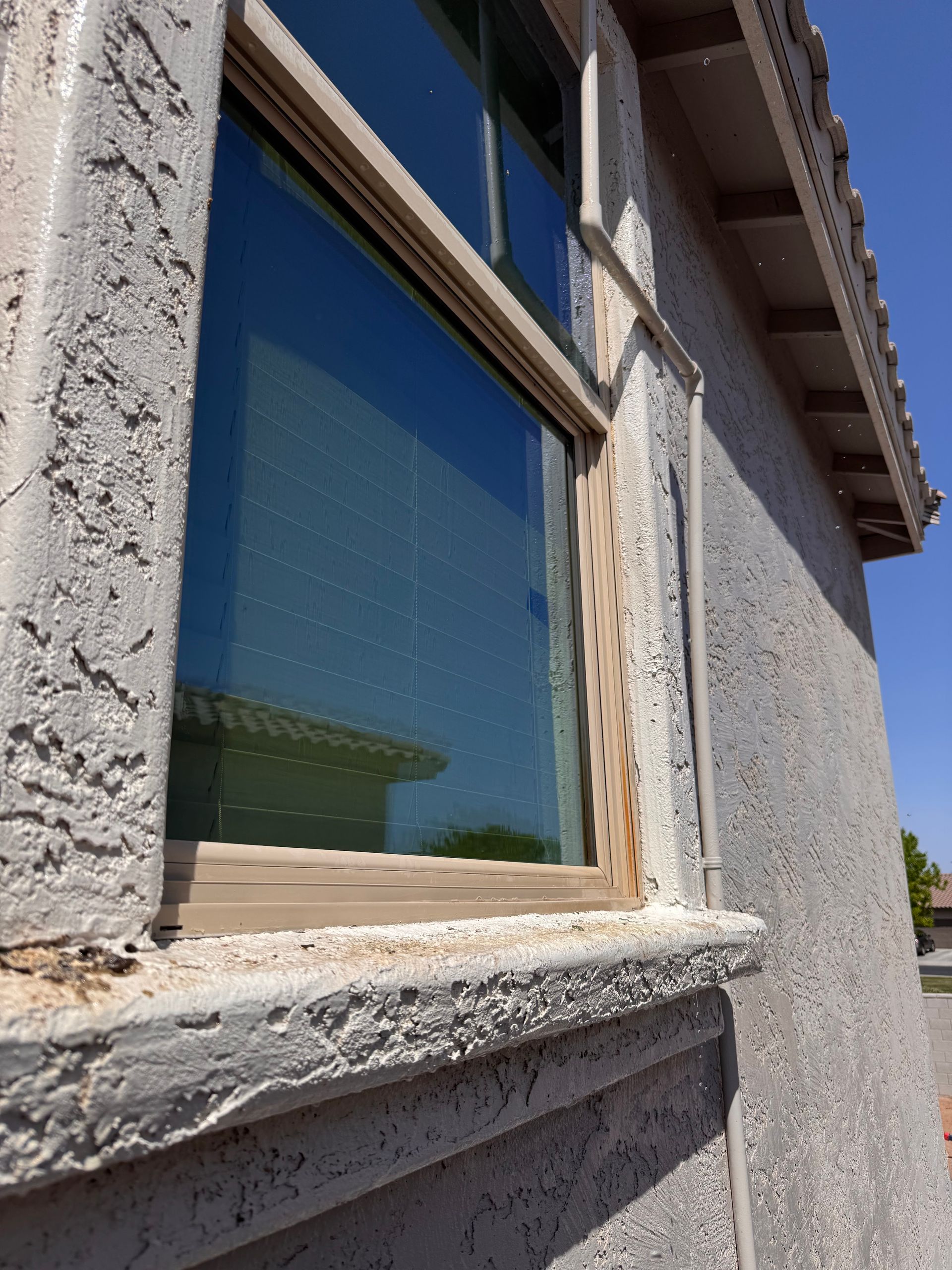 Window with stucco siding and a wooden frame, reflecting the sky and a building.