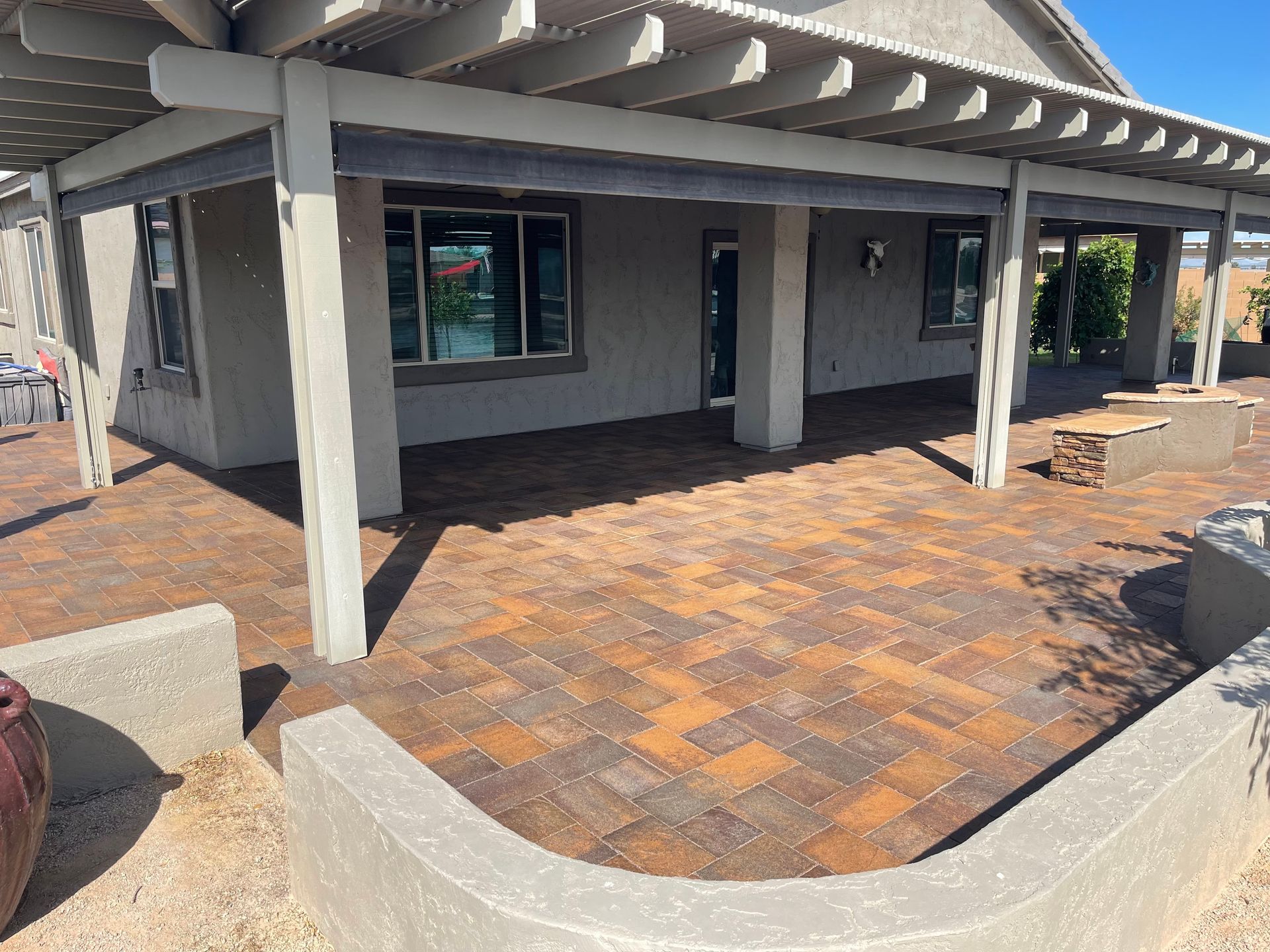 Patio with brick pavers, under a pergola, adjacent to a stucco-walled house.