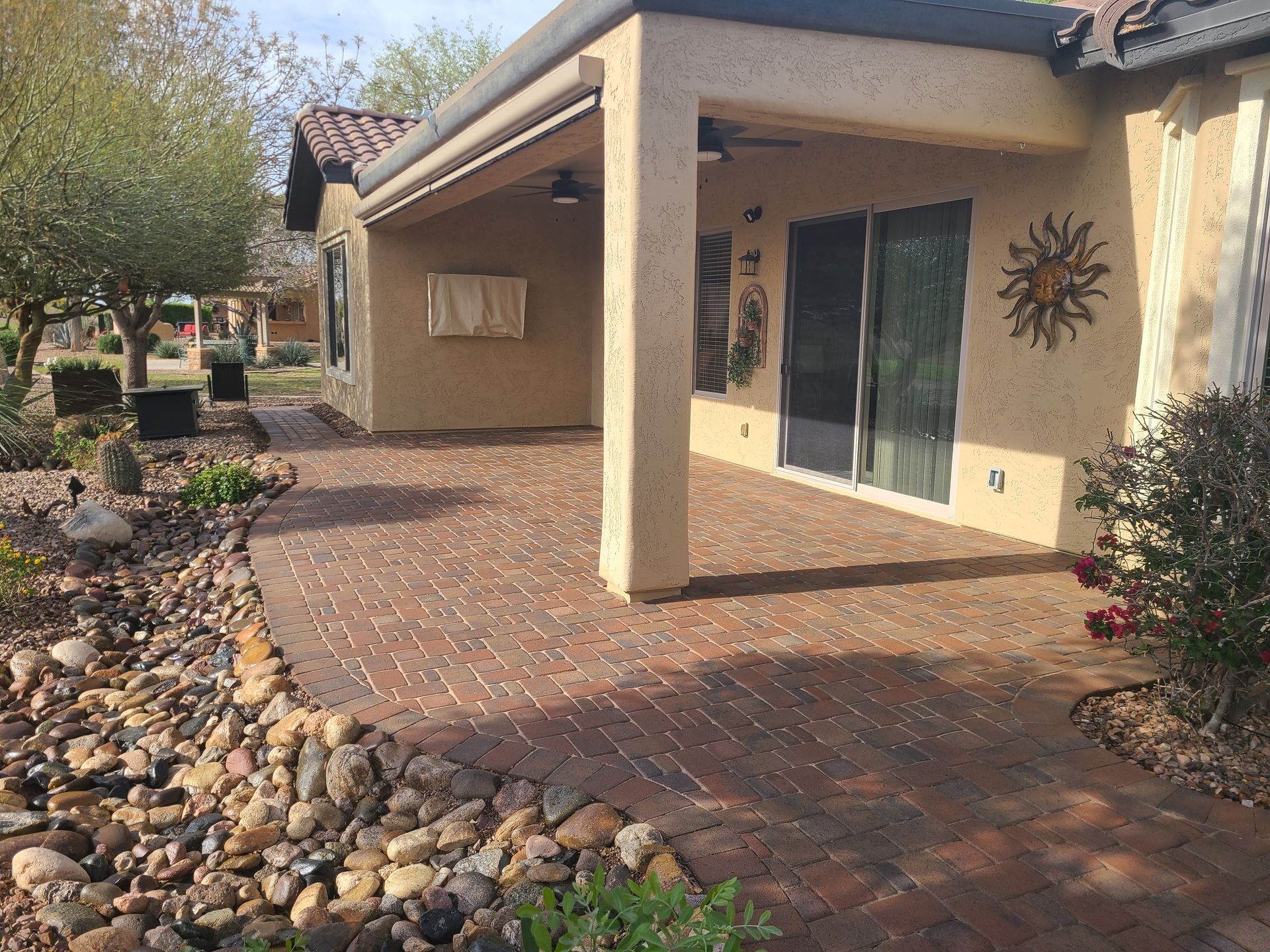 Brick patio with covered area, landscaping, and building.
