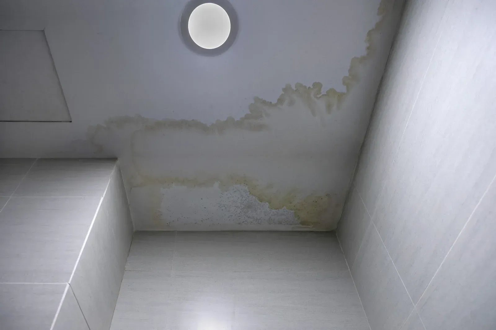 Yellow water stains on a white bathroom ceiling near a light fixture.