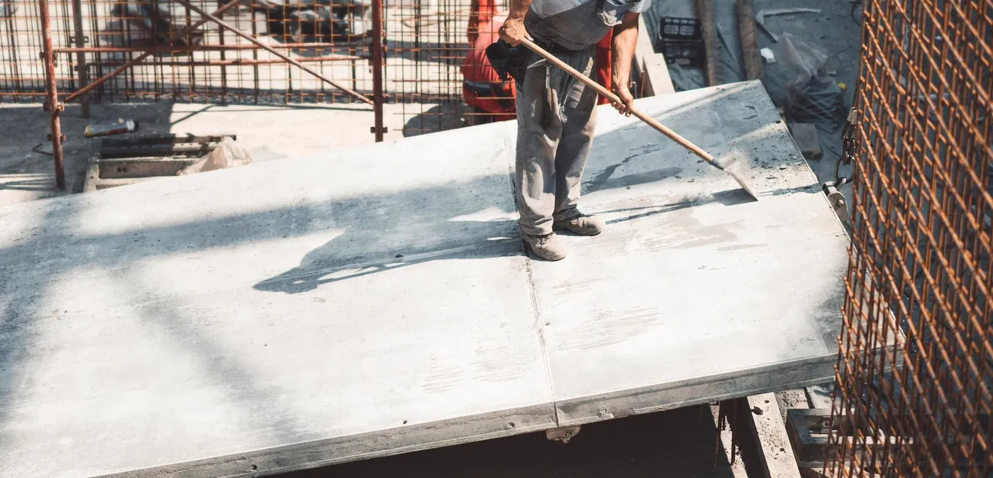 A construction worker smoothing concrete on a large slab.