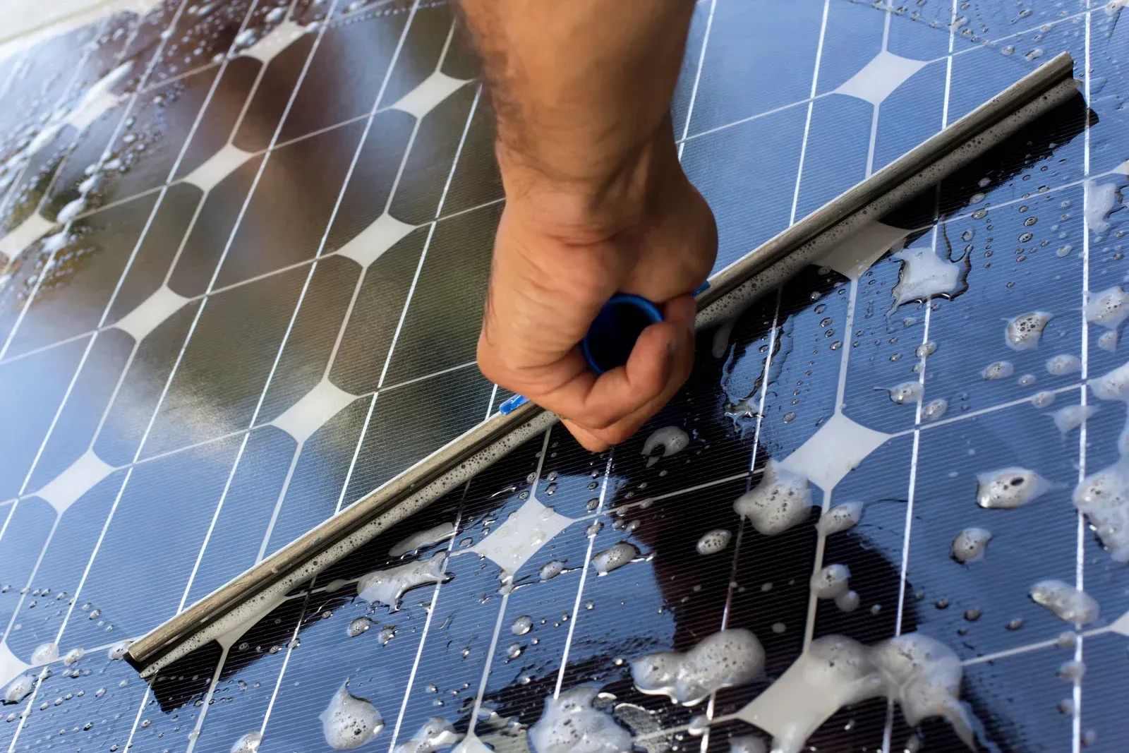 Person cleaning a solar panel with soapy water using a squeegee.