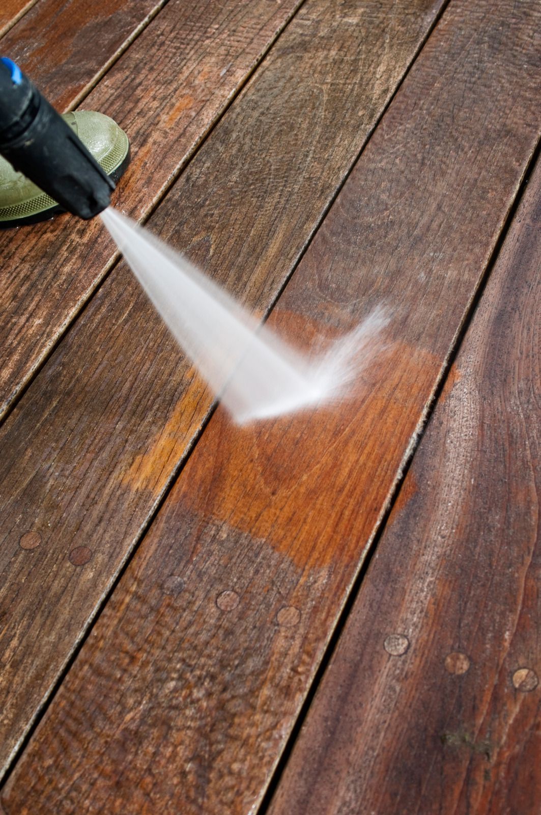 Power washer spraying water on weathered wooden deck.