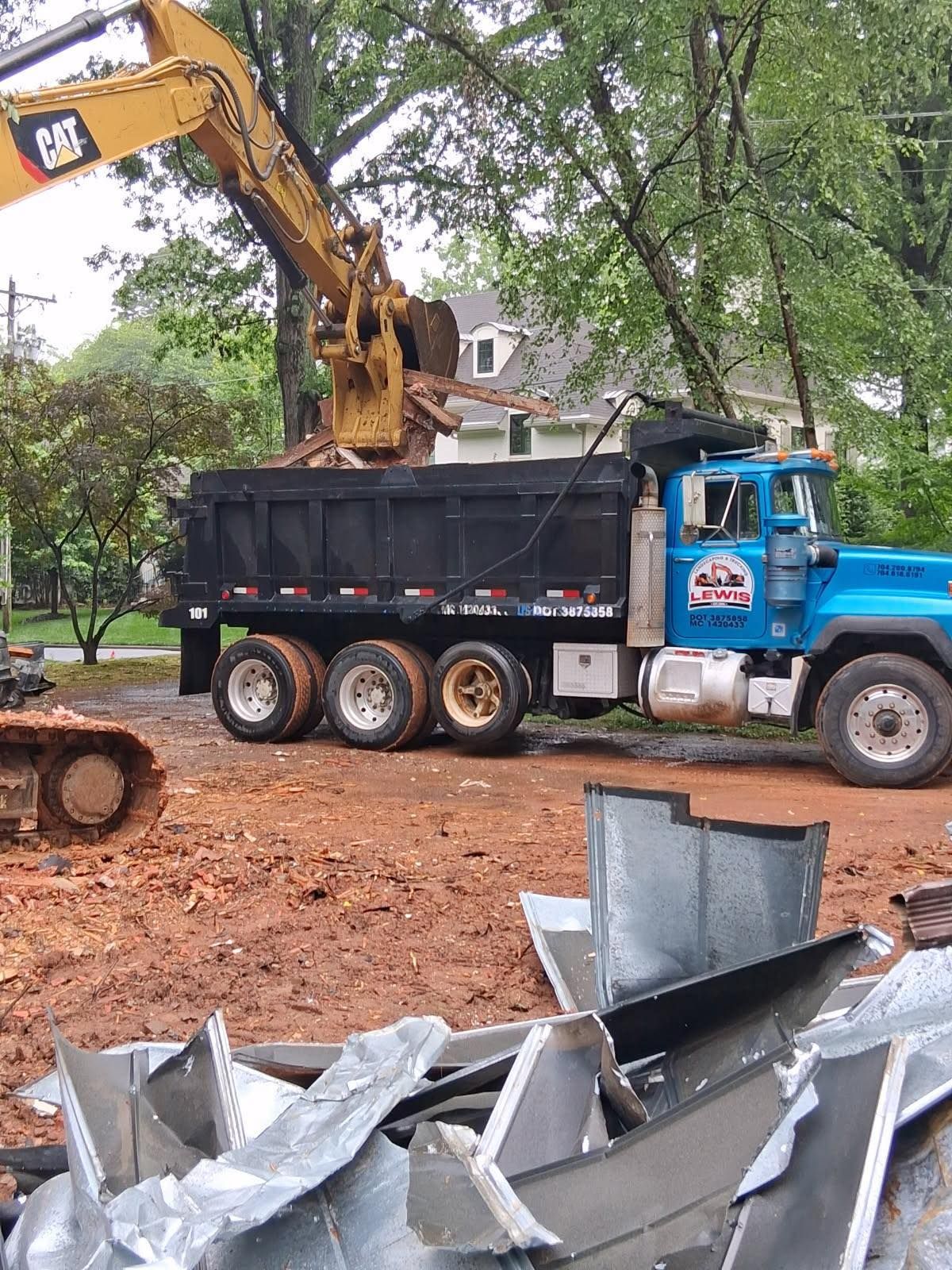 Yellow excavator removing debris and placing into bed of blue dump truck