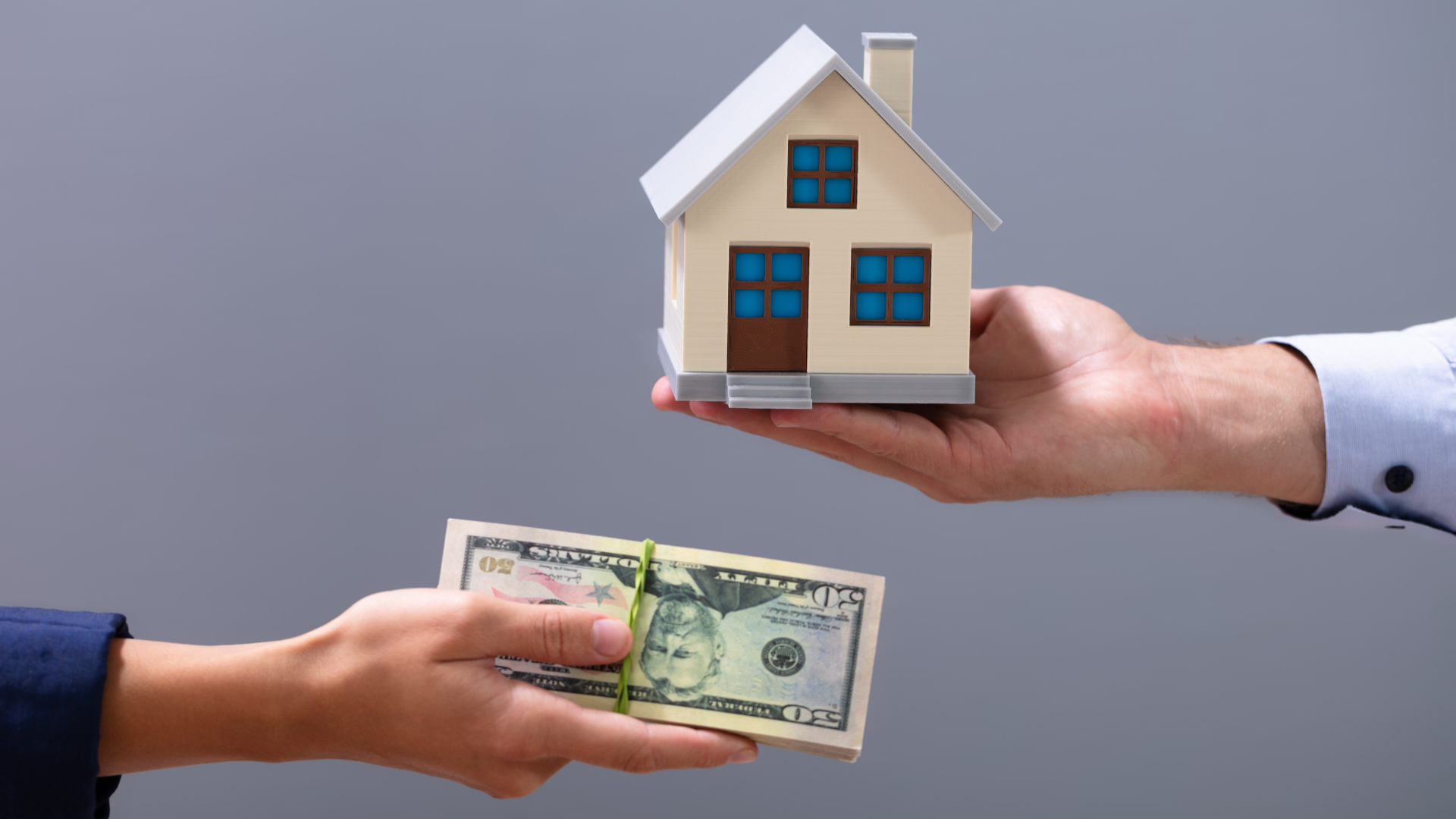 A man is handing a woman a model house and a bunch of money.