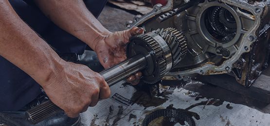 Person holding a gear shaft assembly, working on a vehicle's transmission.